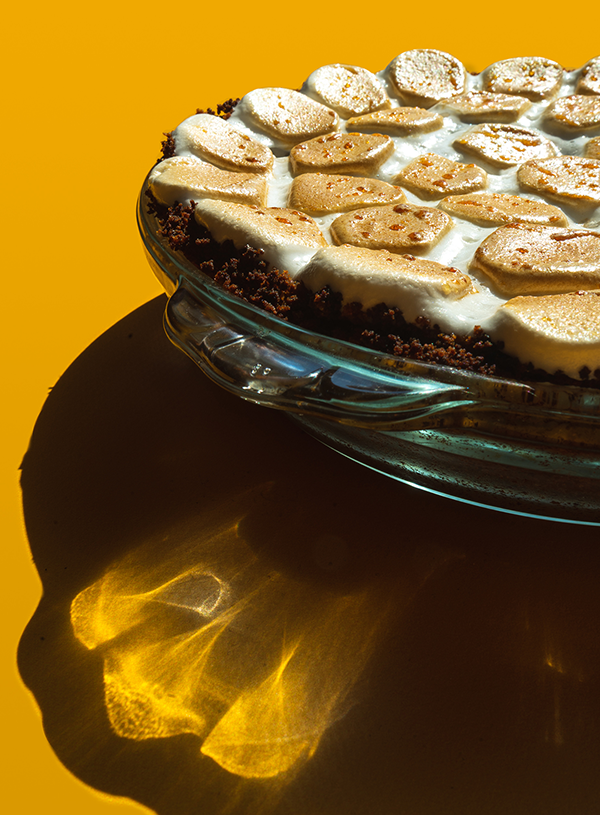 Een close-up van een smores pie bedekt met gebrande marshmallows op een gele achtergrond.