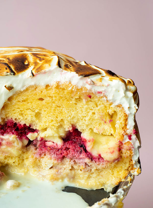 Een closeup dwarsdoorsnede van pastel tres leches met een laag cake, daarop een laag framboze en melk kruim, daarop weer een laag cake, omhult in een laag gebrande meringue.